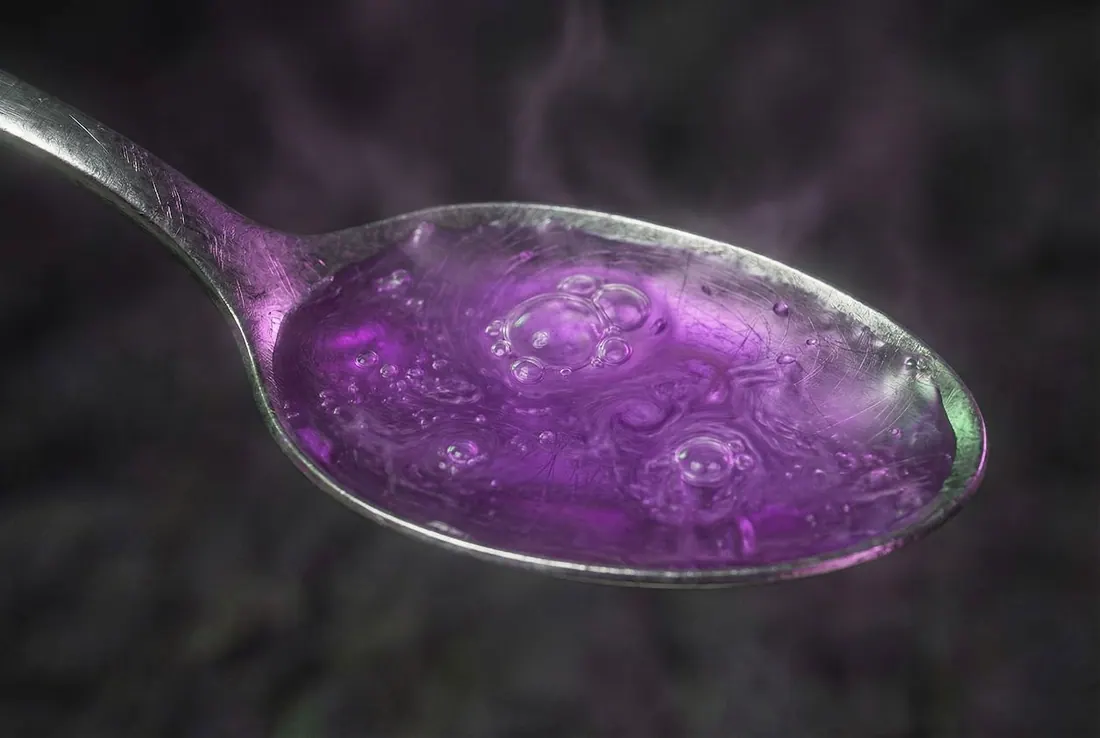 A close-up of a bubbling purple potion in a metal spoon